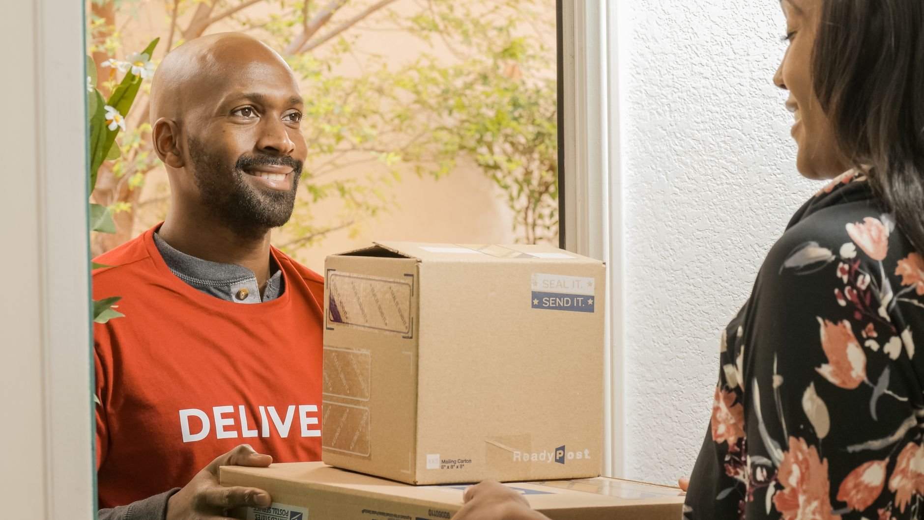 Delivery person handing a package to a smiling recipient at the door
