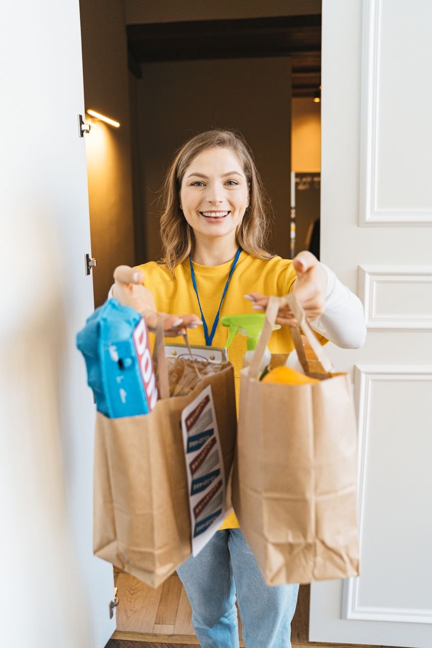 Smiling woman holding grocery bags at her front door — a happy Clurely customer